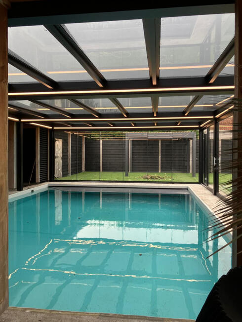 Überdachter Poolbereich mit Aluminiumkonstruktion und großflächigen Glasschiebeelementen